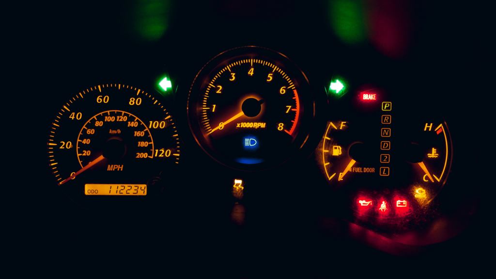 Photograph of a car dashboard with all the indicator lights showing red and orange, including check engine, low oil, fuel tank on empty.