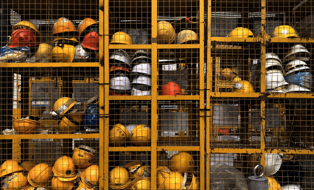 Photograph of a yellow cage holding many stacked cubbies storing a variety of safety hardhats
