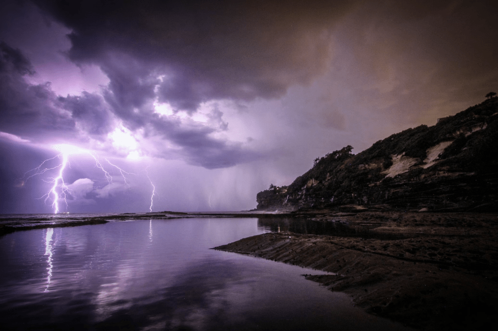 Photo by Jeremy Bishop on Unsplash. Color photo of lightning and thunderclouds over a bay.