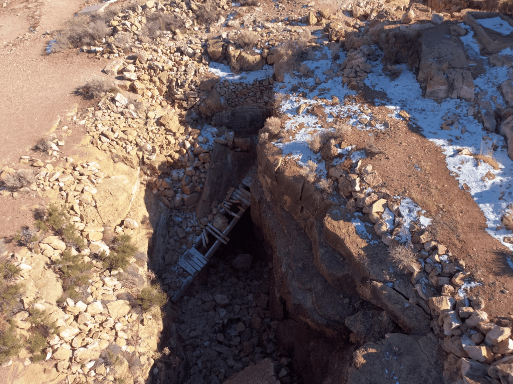Photo by Strange Happenings on Unsplash. Color photo taken from above of a collapsed mine under snowy, stone ground with a broken wooden bridge inside. 

